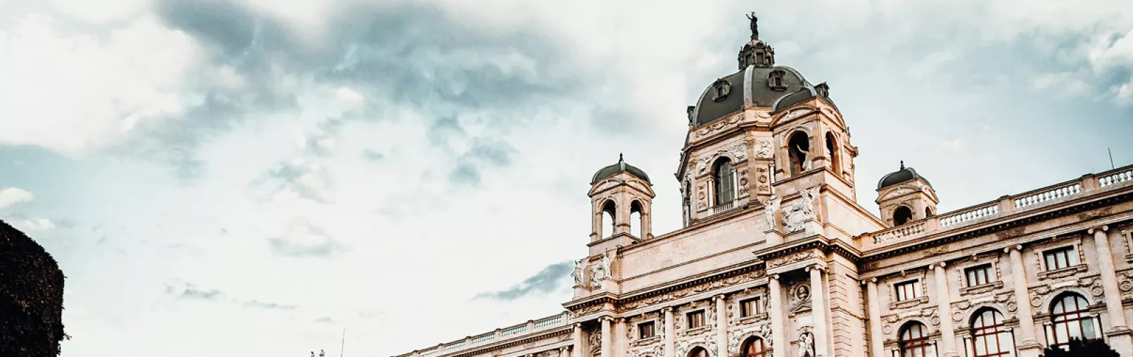 Exterior view of a grand historic European building with ornate architecture under a cloudy sky.