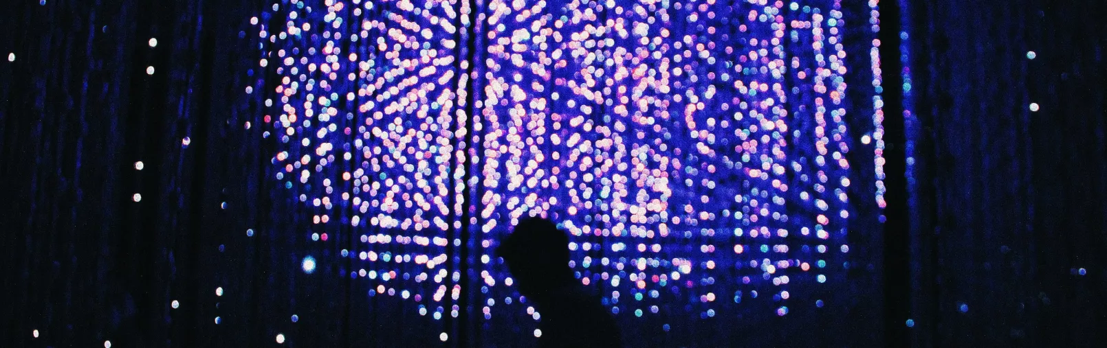 Silhouette of a person standing in front of a large immersive installation of glowing blue and purple lights.