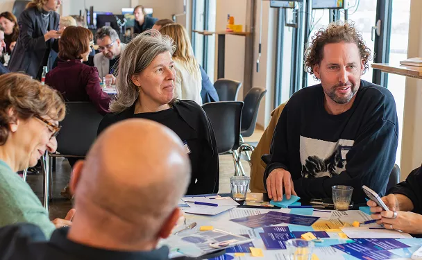 People seated around a table during a workshop or meeting, engaged in discussion with notes and materials spread out in front of them.