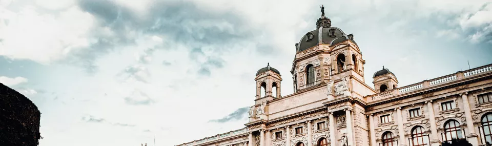Exterior view of a grand historic European building with ornate architecture under a cloudy sky.