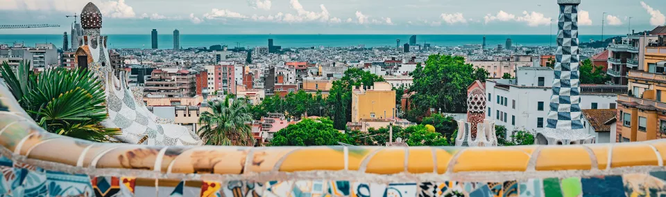 Panoramic view of Barcelona from Park Güell, showing colourful mosaic architecture in the foreground and the city stretching toward the sea.