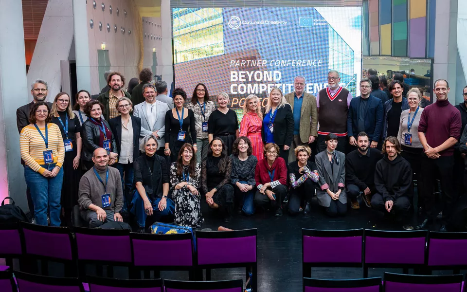 A large group of participants posing together for a group photo at a conference, standing in front of a screen displaying the event title.